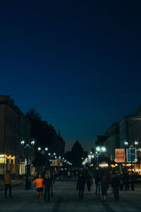 People walking on illuminated street amidst buildings at night