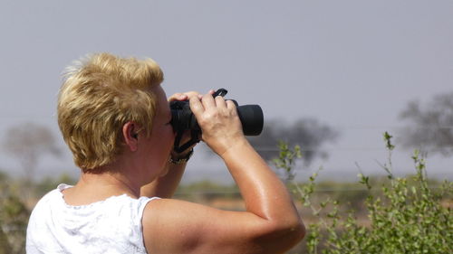 Woman looking through binoculars against sky