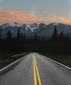 Empty road leading towards mountains against sky during sunset