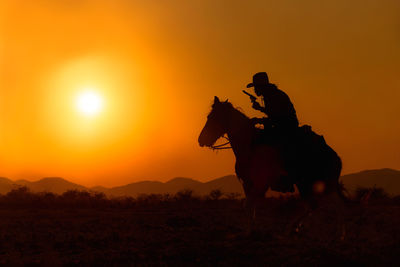 Silhouette riding horse on field against orange sky