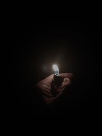Hand holding lit candle in darkroom