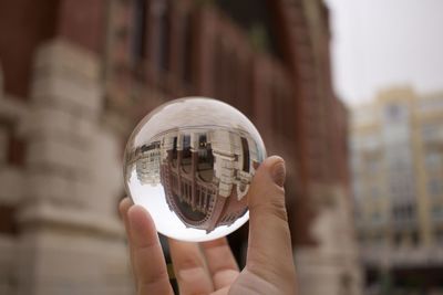 Midsection of person holding crystal ball on glass of building
