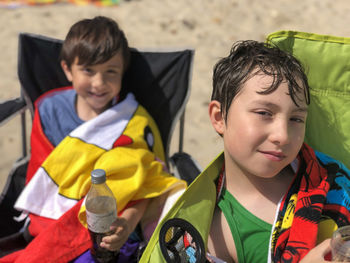 Portrait of smiling cute siblings sitting on chair at beach