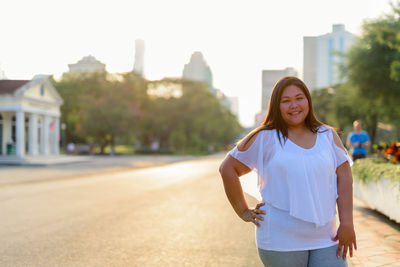 Portrait of smiling young woman standing against sky in city