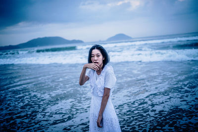 Young woman standing at beach against sky