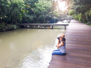 Rear view of woman sitting on bench by trees