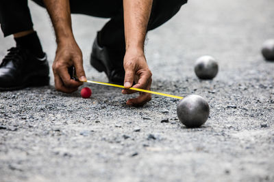 Low section of man measuring metallic sphere on land