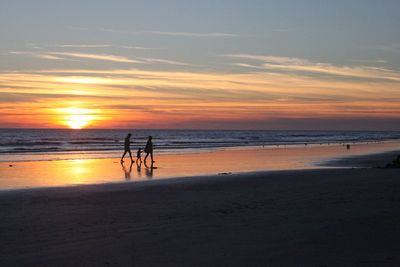 Silhouette people standing on beach against sky during sunset