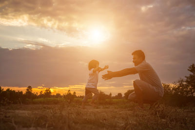 Father and son on field against sky during sunset