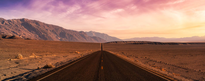 Road leading towards desert against sky during sunset