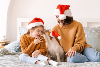 Happy family have fun with funny dog on bed in santa hats. emotional moments.