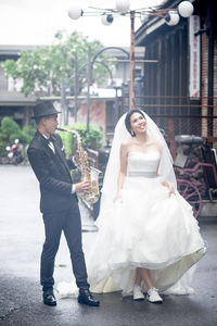Full length of man playing saxophone while bride walking on road
