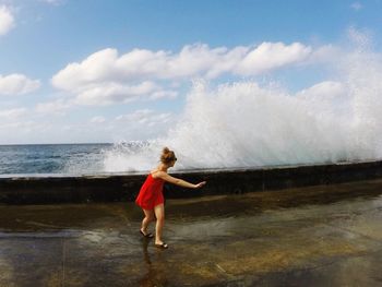 Full length of woman running from splashed waves against sky