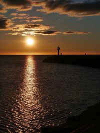 Silhouette of lighthouse in sea during sunset