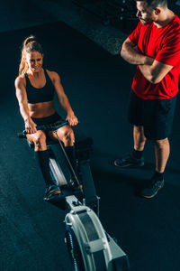 High angle view of coach standing by woman exercising at gym