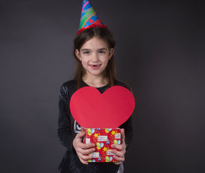 Portrait of smiling woman holding heart shape against gray background