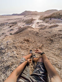 Low section of people relaxing on land against sky