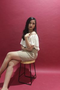 Young woman looking away while sitting on table over red background