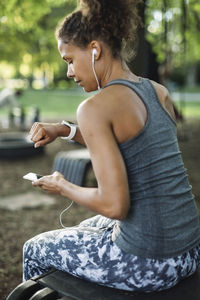 Woman using smart phone and looking at wristwatch in park