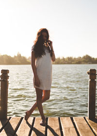 Young woman standing on pier over lake against sky