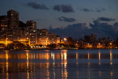 Illuminated buildings by sea against sky at night