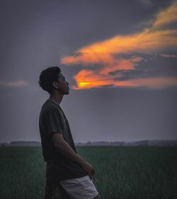 Man kneeling on field against sky during sunset