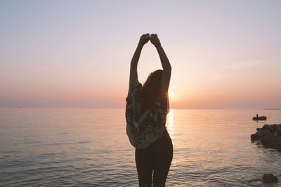 Back view of woman standing with hands above her head by the shore