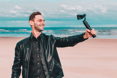 Smiling young man filming with video camera at beach