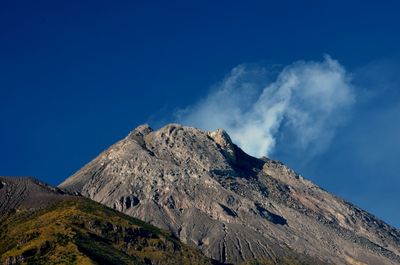 Low angle view of volcanic mountain against blue sky