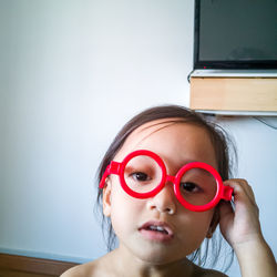Happy toddler girl playing with red fake sunglasses at home.