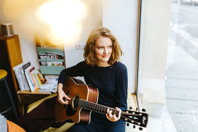 High angle view of young woman playing guitar by window at home