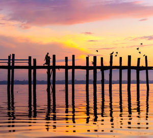 Silhouette wooden posts on sea against orange sky
