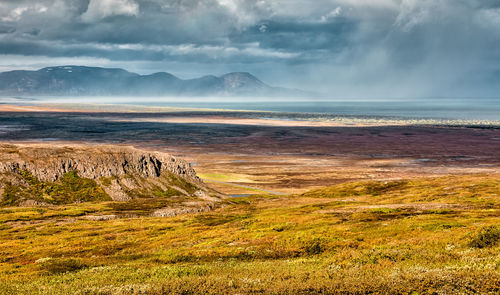 Scenic view of landscape in front of stormy sea against turbulent sky