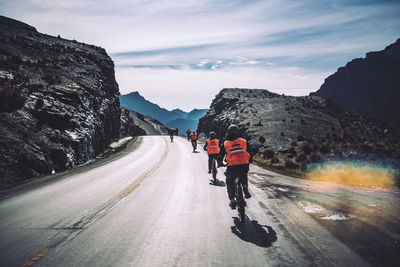 Rear view of people riding motorcycle on road against sky