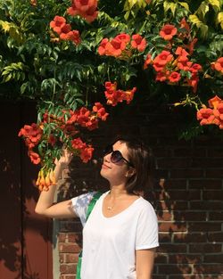 Young woman smelling orange flowers blooming by brick wall