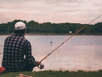 Man fishing in lake against sky