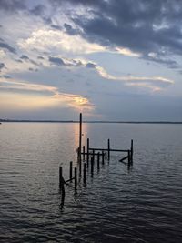 Silhouette wooden posts in sea against sky at sunset