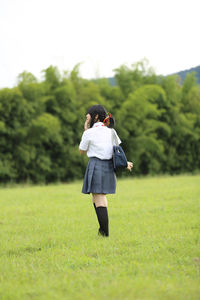 Rear view of woman in school uniform walking on field