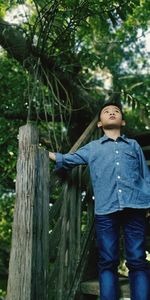 Boy looking away while standing against tree