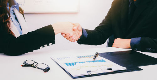 Midsection of business colleagues shaking hands while sitting at desk in office