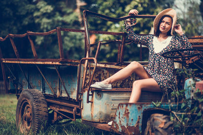 Portrait of young woman sitting on abandoned vehicle at field