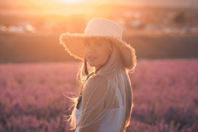 Beautiful smiling woman wear straw hat and dress standing in purple lavender flower field outdoor