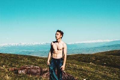 Shirtless man standing at lake against sky