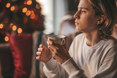 Portrait of candid authentic smiling handsome boy teenager using mobile phone at xmas home interior