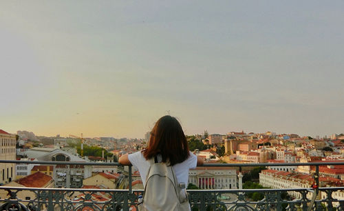 Rear view of woman standing on balcony against buildings in city