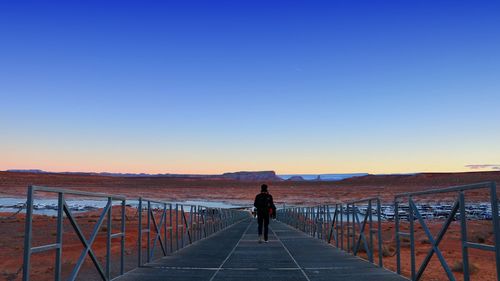 Woman walking on bridge against clear sky