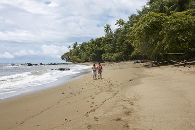 Rear view of woman walking at beach against sky