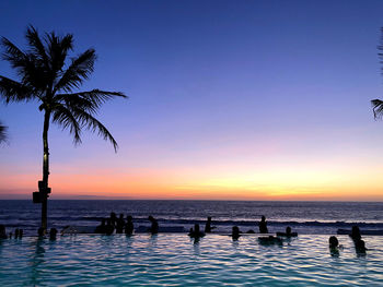 Silhouette people by swimming pool against sky during sunset