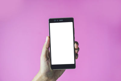 Low section of person holding smart phone against pink background