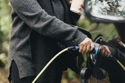 Midsection of mid adult woman charging electric car